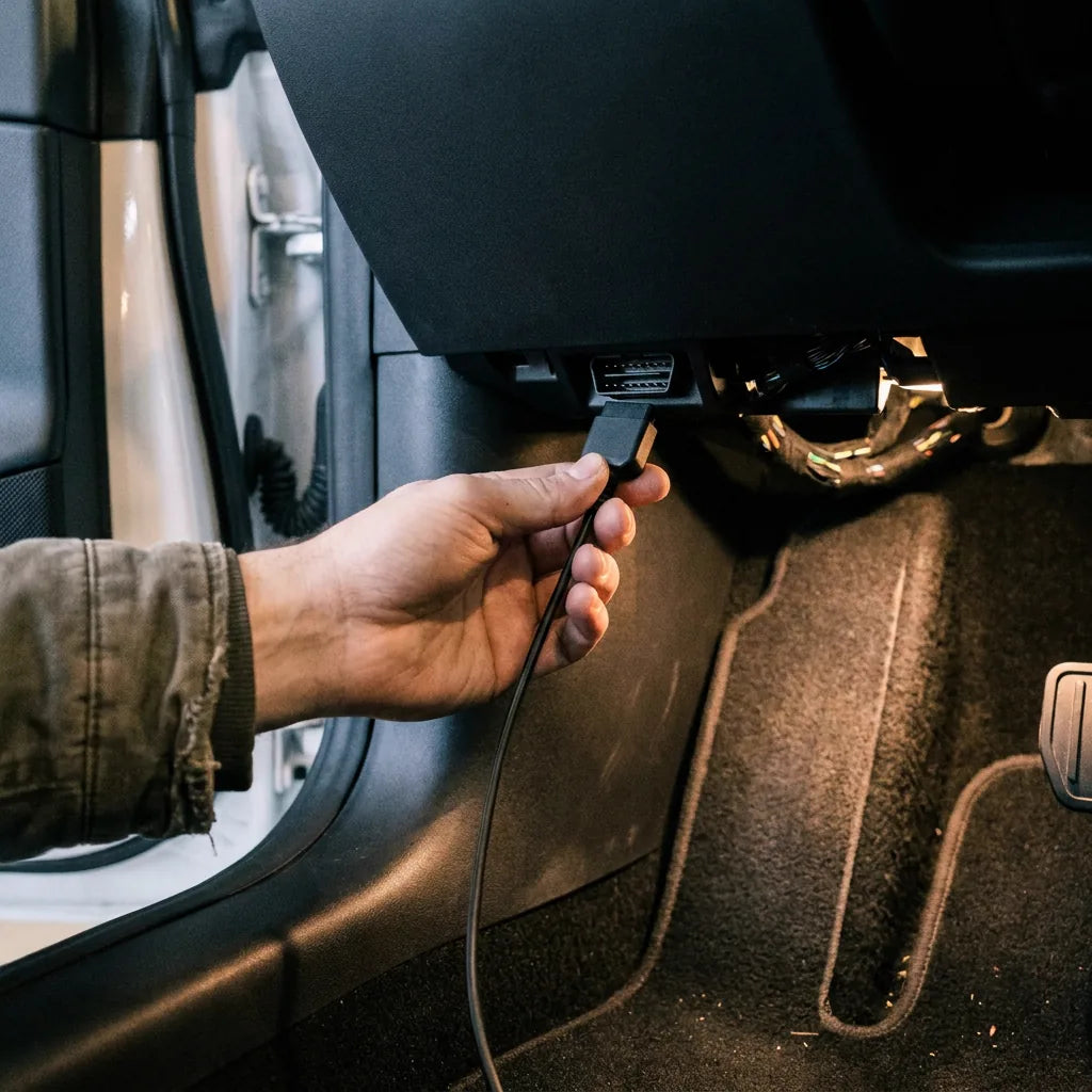 Main présentant le connecteur du câble d'alimentation à la prise de diagnostic, sous la planche de bord côté conducteur